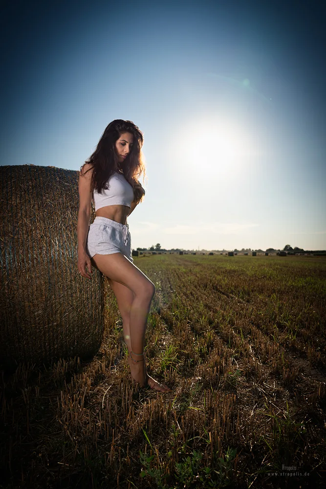 A woman in shorts stands in a summer field against the low sun
