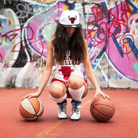 A woman crouching on a basketball court in front of graffiti