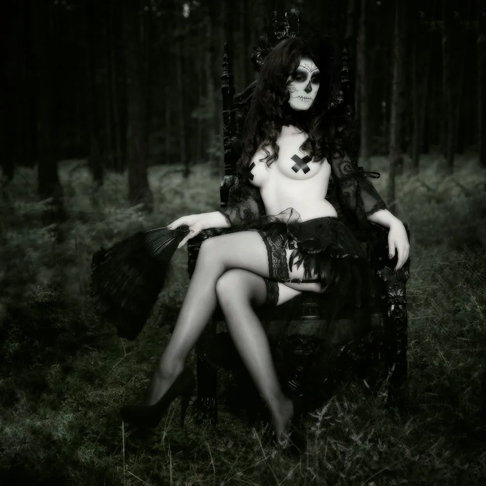 A woman with sugar skull make-up on a throne in a dark forest